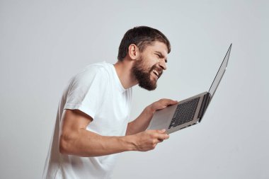 Elinde dizüstü bilgisayarla beyaz tişörtlü bir arka planı olan bir adamın duyguları yeni teknolojileri aydınlatır.