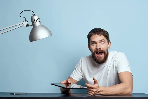 Homem com tablet à mesa dentro de casa e lâmpada escritório freelancer fundo azul — Fotografia de Stock