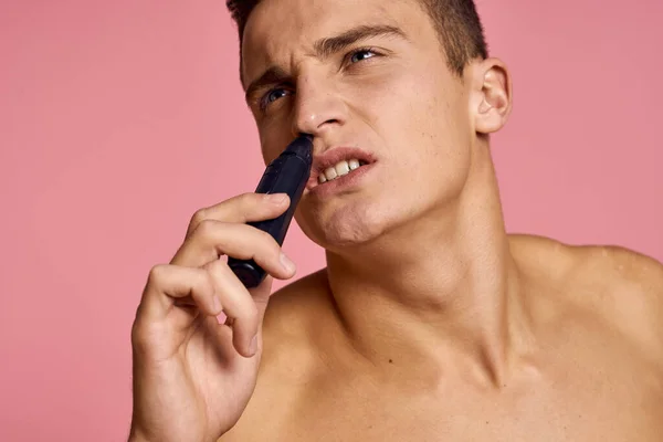 Bello uomo con un trimmer nella sua mano depilazione macchina rosa sfondo nudo torso — Foto Stock