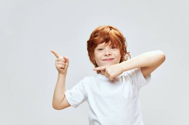 Neşeli kızıl saçlı çocuk elleriyle işaret parmaklarını yana doğru gösteriyor. 