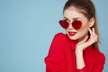 Mavi arka plandaki kırmızı gömlekli kadın yüz ve güneş gözlüklü kırmızı dudak makyajı modeli ile el ele tutuşuyor.