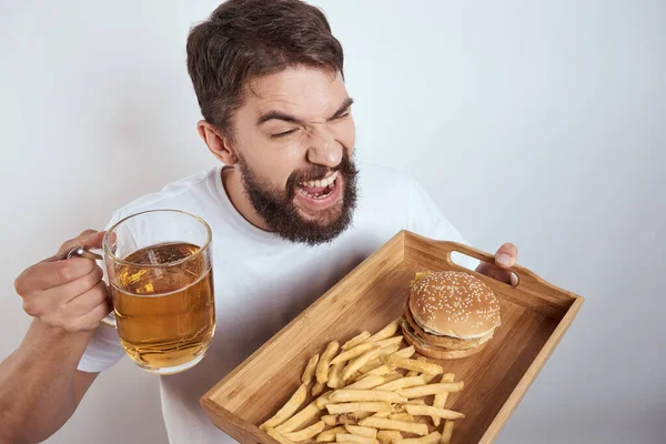 Homem com bandeja de madeira caneca de cerveja batatas fritas e hambúrguer fast food calorias modelo branco t-shirt — Fotografia de Stock