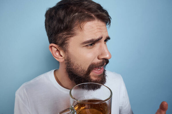 Cheerful man in a white T-shirt with a beer mug drunk blue background