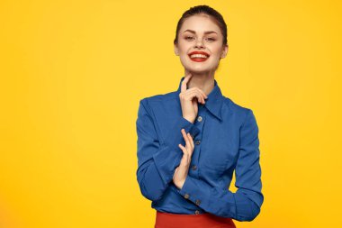 Mavi gömlekli, parlak makyajlı, kırmızı dudaklı, sarı arkaplan manzaralı bir kadın portresi