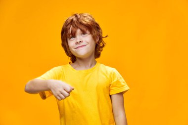 Sarı arka planda kızıl saçlı rüya gibi bir çocuk elini yüzünün önünde tutuyor. 