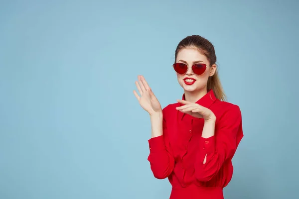 Mulher de camisa vermelha no fundo azul segura as mãos perto do rosto e óculos de sol modelo de maquiagem lábios vermelhos — Fotografia de Stock