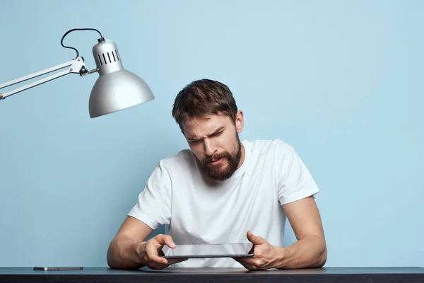 Homem com tablet à mesa dentro de casa e lâmpada escritório freelancer fundo azul — Fotografia de Stock