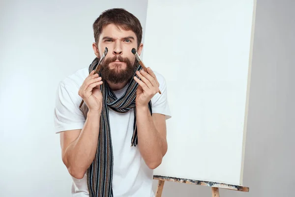 Pincel de artista masculino en manos de pasatiempo arte caballete bufanda de fondo ligero alrededor de su cuello — Foto de Stock
