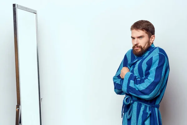 Um homem em um manto azul examina-se em um espelho em uma sala brilhante vista cortada — Fotografia de Stock