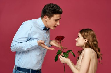 Pembe arka planda kırmızı çiçekli aşık bir adam ve kadın birbirlerine sarılırlar.