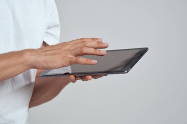 Açık arkaplanda dokunmatik ekranlı tablet erkek elleri beyaz tişört kırpılmış görünüm