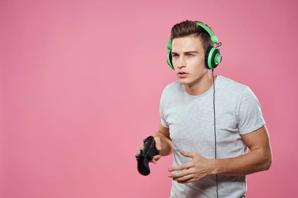 Een man met een joystick in zijn handen koptelefoon spelen spelletjes entertainment levensstijl wit t-shirt roze achtergrond — Stockfoto