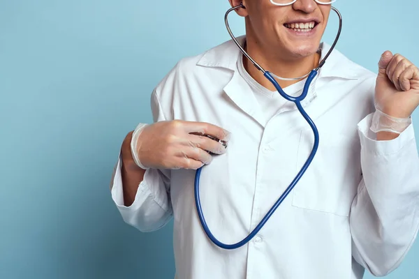 Un trabajador médico con una bata y gafas sostiene un estetoscopio en sus manos sobre un fondo azul vista recortada —  Fotos de Stock