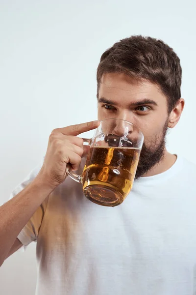 一个留着胡子的男人，带着一大杯啤酒，背景浅淡的，穿着白色T恤，带着酒精饮料的景象 — 图库照片