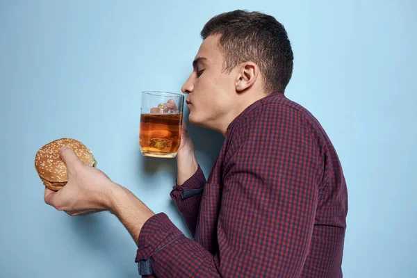 Bira bardağı ve hamburgerli neşeli sarhoş adam. Diyet yemek yaşam tarzı mavi arka plan. — Stok fotoğraf
