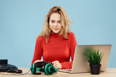 Dizüstü bilgisayar kulaklığının önündeki masada oturan bir kadın çevrimiçi yaşam tarzı mavi arka planda oynuyor.