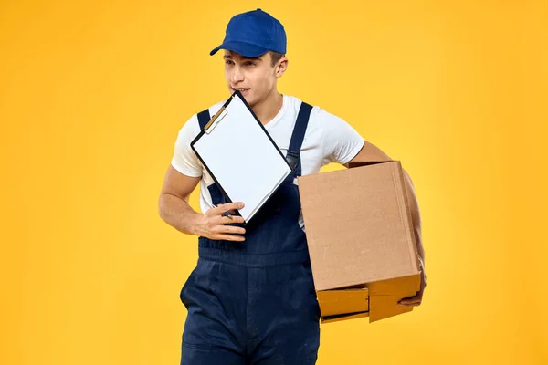 Рабочий в форме с коробкой ручной доставки службы погрузки желтый фон — стоковое фото