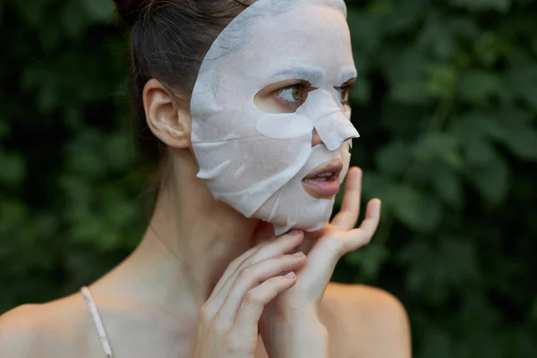 Belle femme tient sa main près de son visage blanc masque soins de la peau feuilles en arrière-plan — Photo