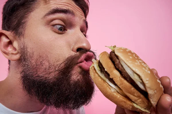 Porträt eines Mannes mit einem Hamburger auf rosa Hintergrund Nahaufnahme ausgeschnittene Ansicht eines Modells — Stockfoto