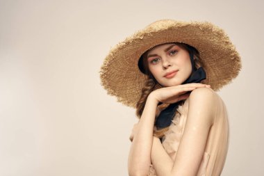 Hasır şapkalı, siyah kurdeleli ve arka planda açık bir elbise giyen hoş bir kız. Romantik bir model.