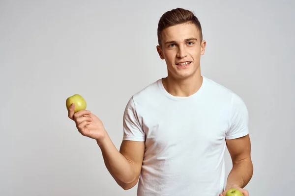 Een man met appels in zijn handen op een lichte achtergrond in een wit t-shirt gesticulate met zijn handen glimlach — Stockfoto