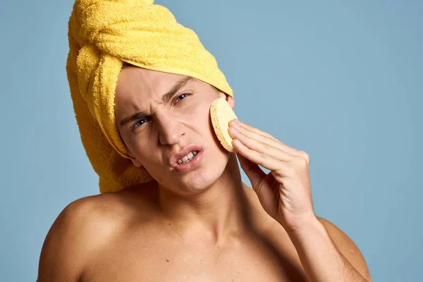 Ein Mann mit einem gelben Handtuch auf dem Kopf und einem weichen Schwamm zur Reinigung des Modells der Hautkosmetologie — Stockfoto