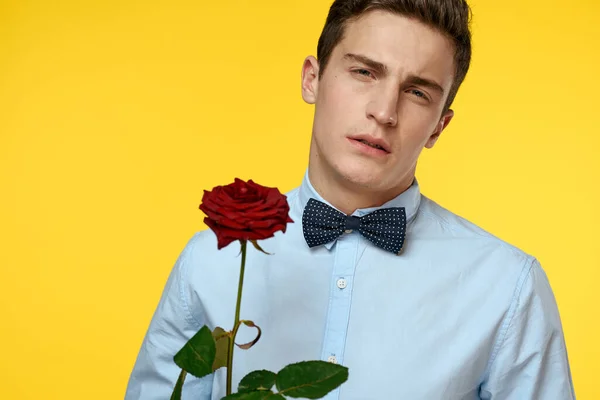 Homme élégant en costume avec une rose rouge dans les mains sur un fond jaune, vue dégagée — Photo