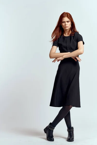 Uma mulher em um vestido preto em um fundo leve e meia-calça sapatos de cabelo vermelho e posar em pleno crescimento — Fotografia de Stock
