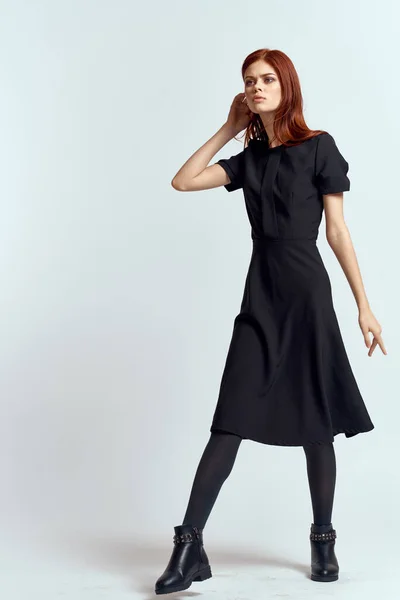 Μια γυναίκα σε ένα μαύρο φόρεμα σε ένα ελαφρύ φόντο και καλσόν παπούτσια κόκκινα μαλλιά και θέτουν σε πλήρη ανάπτυξη — Φωτογραφία Αρχείου