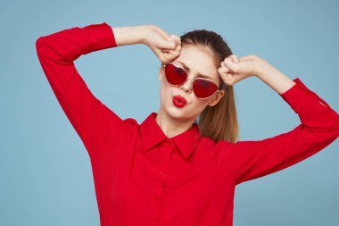 Koyu renk gözlüklü, kırmızı gömlekli, parlak makyajlı çekici bir kadın.