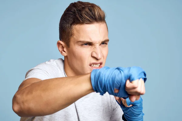 Hombre deportivo en guantes de boxeo azul y camiseta sobre fondo azul practicando golpes vista recortada — Foto de Stock
