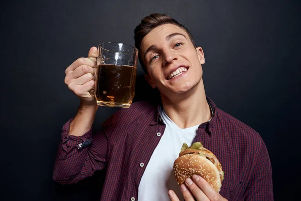 Homme avec tasse de bière et hamburger dans les mains style de vie amusant studio sombre fond isolé — Photo