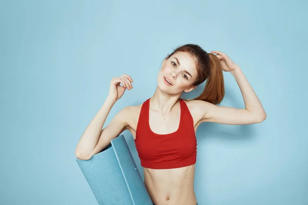 Sportiv kvinna träningsmatta i händer Röd tank övning blå bakgrund — Stockfoto
