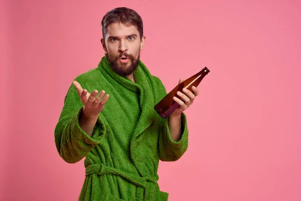 Homem bêbado com uma garrafa de álcool na mão em um fundo rosa vista cortada de um manto verde — Fotografia de Stock