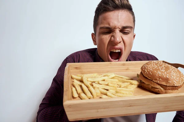 Önünde bir palet dolusu fast food patates kızartması ve yakın plan hamburger yiyen bir adam var. — Stok fotoğraf