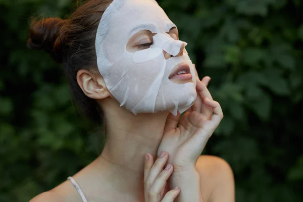 Leuke vrouw wit masker Houdt zijn hand in de buurt van zijn gezicht dermatologie bladeren op de achtergrond — Stockfoto
