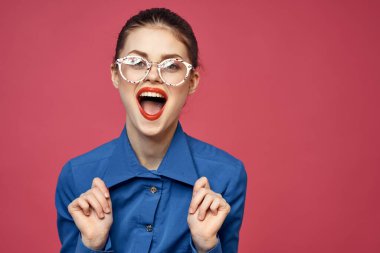 Gözlüklü ve mavi gömlekli bir kadının portresi. Kırmızı dudaklı, pembe arka plan modeli.