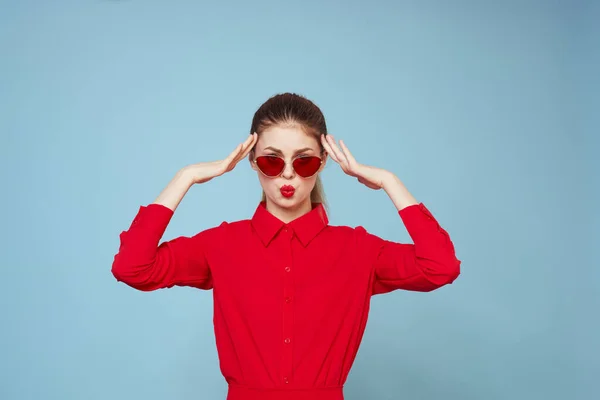 Donna in camicia rossa su sfondo blu tiene le mani vicino al viso e occhiali da sole modello di trucco labbra rosse — Foto Stock