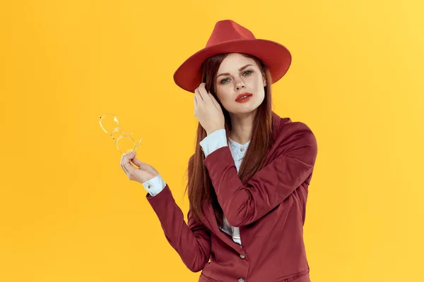 Mujer en rojo sombrero chaqueta gafas amarillo fondo cosméticos — Foto de Stock