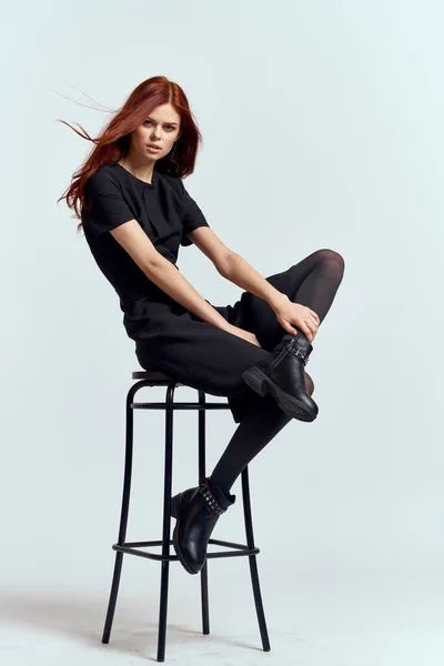 Mulher alta cadeira em casa comprimento total vestido preto vermelho cabelo modelo botas — Fotografia de Stock