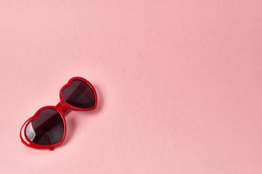 Kalp şeklinde güneş gözlüğü, pembe arkaplanda kırmızı çerçeveler.