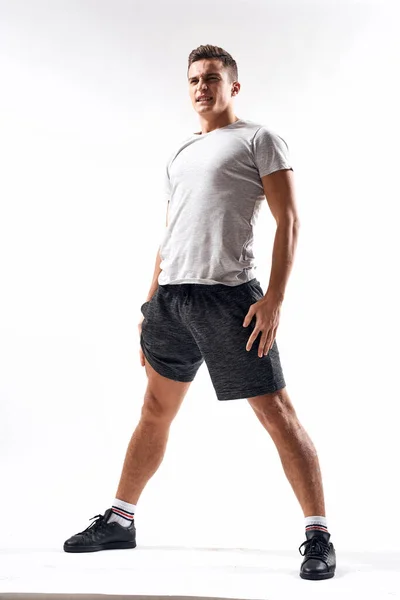 Un hombre deportivo en pantalones cortos y una camiseta larga hace ejercicios sobre un fondo claro — Foto de Stock