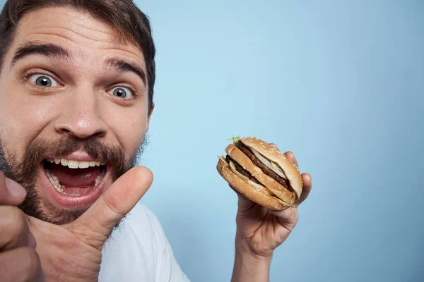 Emocionální člověk hamburger fast food strava jídlo close-up modré pozadí — Stock fotografie