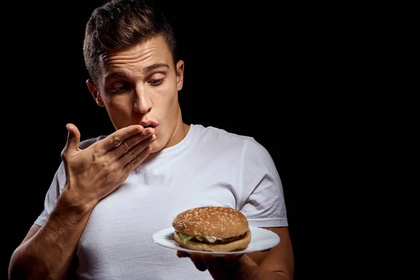 Hombre con platos de hamburguesas sobre fondo negro en camiseta blanca retrato recortado vista de comida rápida — Foto de Stock