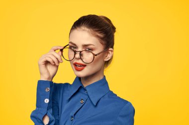 Mavi gömlekli, gözlüklü, yüzünde parlak makyajlı bir kadın elleriyle işaret ediyor.