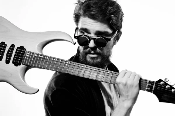 A man holds a guitar in his hands black leather jacket dark glasses music performance light background