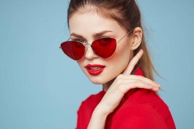 Koyu gözlükleri olan güzel bir kadın parlak makyajlı kırmızı dudaklar mavi arkaplanı büyülüyor.