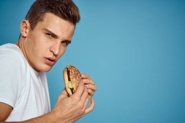 Hamburger ve beyaz tişörtlü adam mavi arkaplan duyguları elleriyle işaret ediyor Boşluğu kopyala