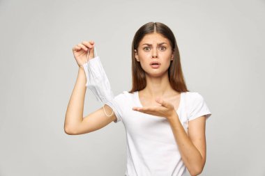 Yüzünde şaşırmış bir ifade, elinde tıbbi bir maske olan bir kadın.