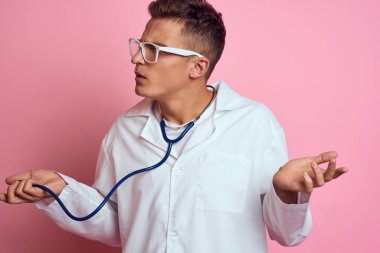 Pembe bir arka planda steteskop ve yüzünde gözlük olan tıbbi önlüklü bir erkek doktor.